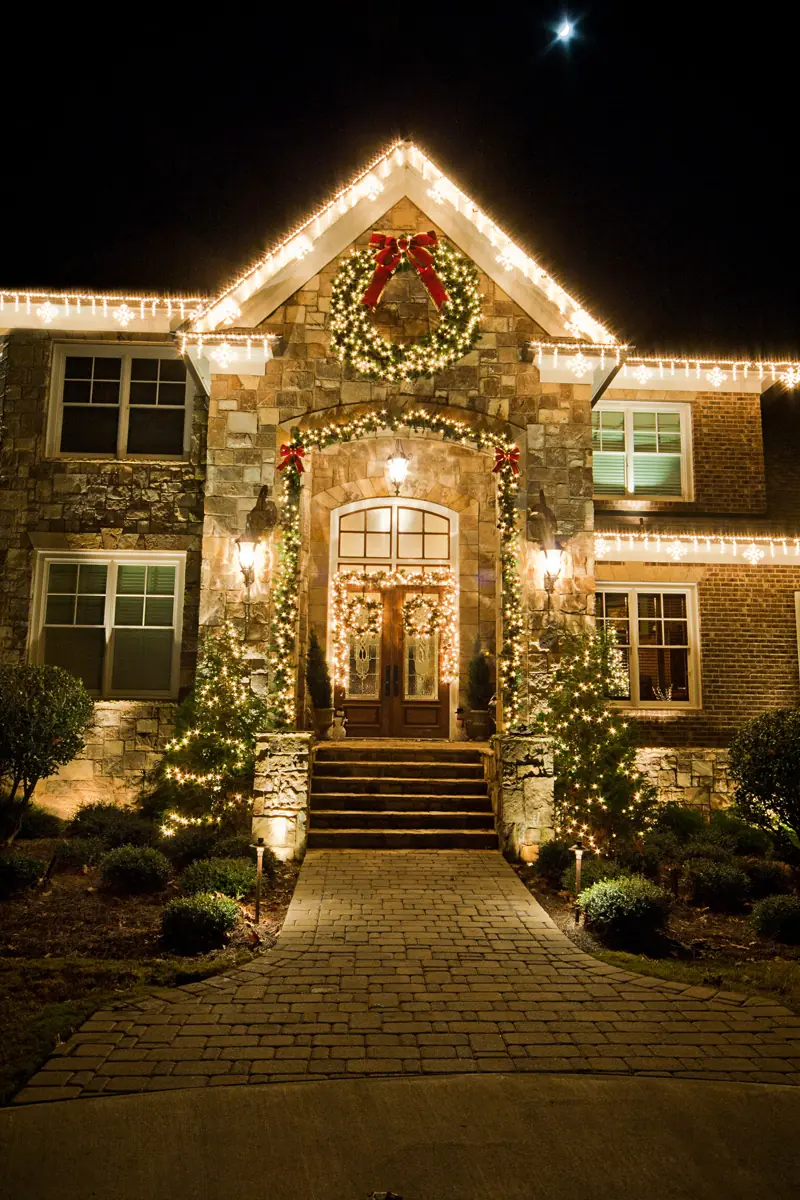 Luxury home entrance decorated with warm roofline lights and seasonal greenery